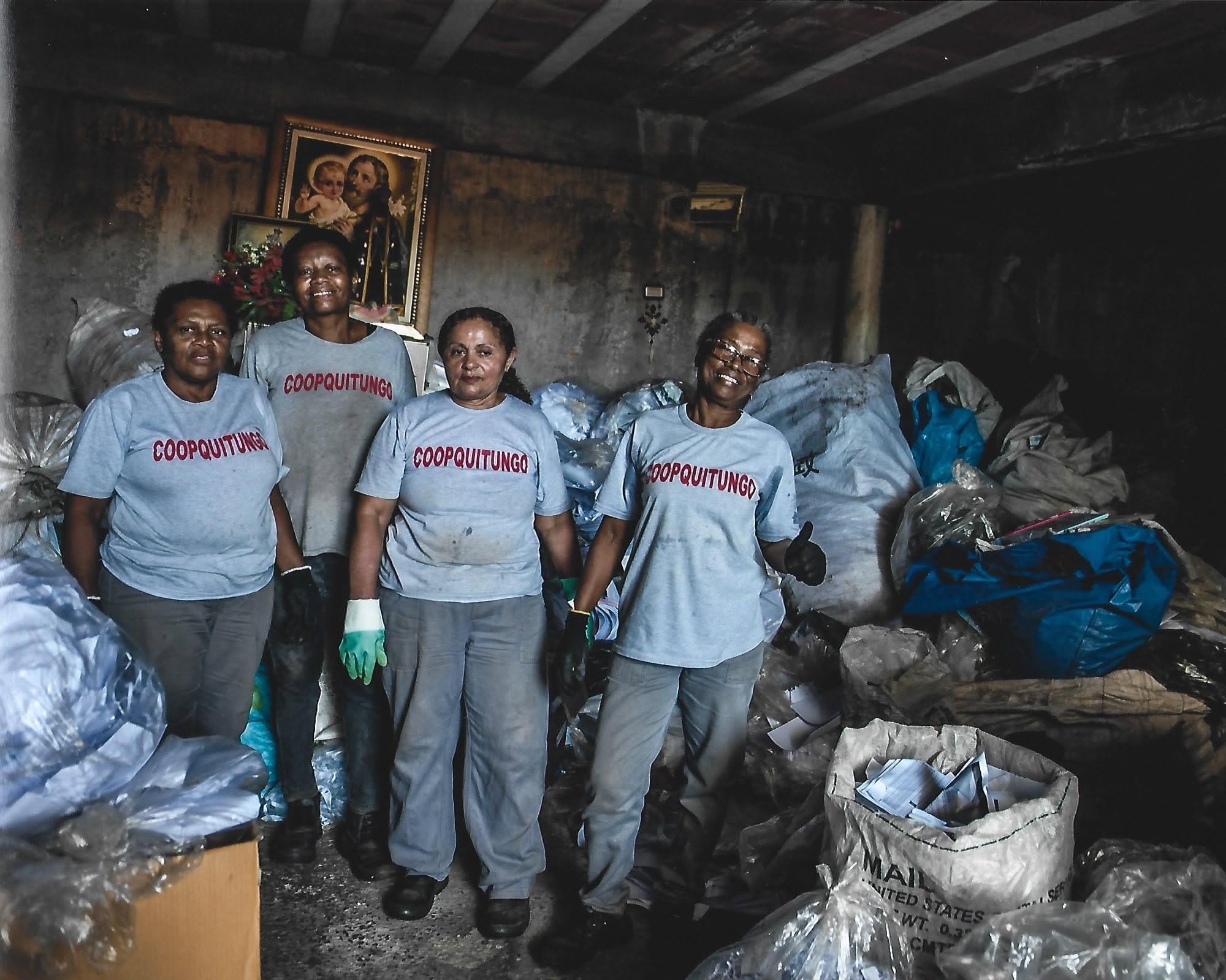Quatro cooperadas da Coopquitungo com camisetas da cooperativa entre sacos de material reciclável